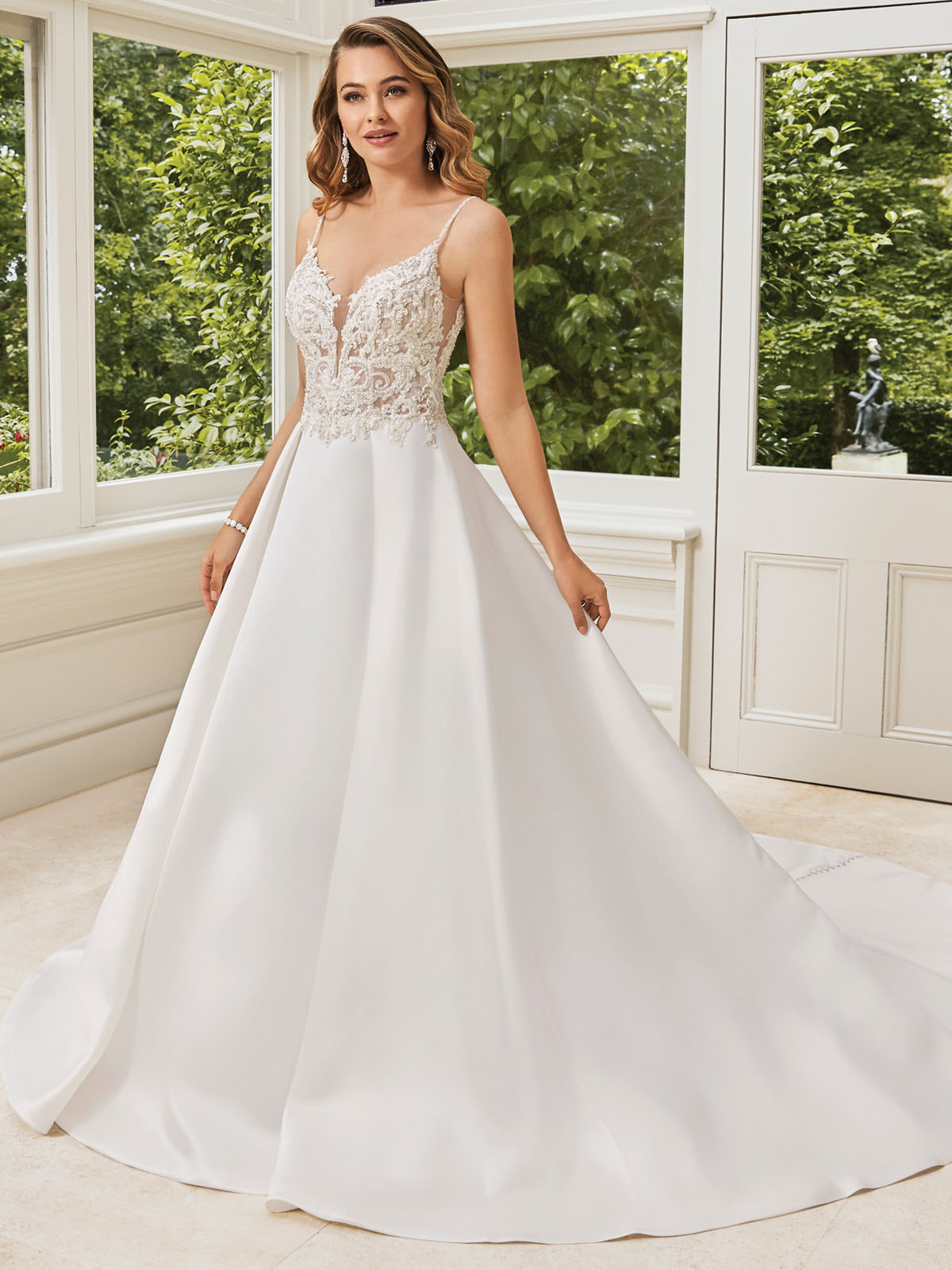 Moderno e elegante, este vestido de linha Mikado de luxo  um sonho tornado realidade, que apresenta um corpete impressionante e semi-transparente de apliques de renda  bordado de  cristal, colocados em cima de uma camada de renda Chantilly, com um decote em V sexy e tule transparentes na frente e nas laterais. A saia completa oferece bolsos laterais de costura para versatilidade e pregas macias para formar volume. costas que levam a um decote em V baixo com zper, enquanto os botes cobertos por Mikado caem em toda cauda.